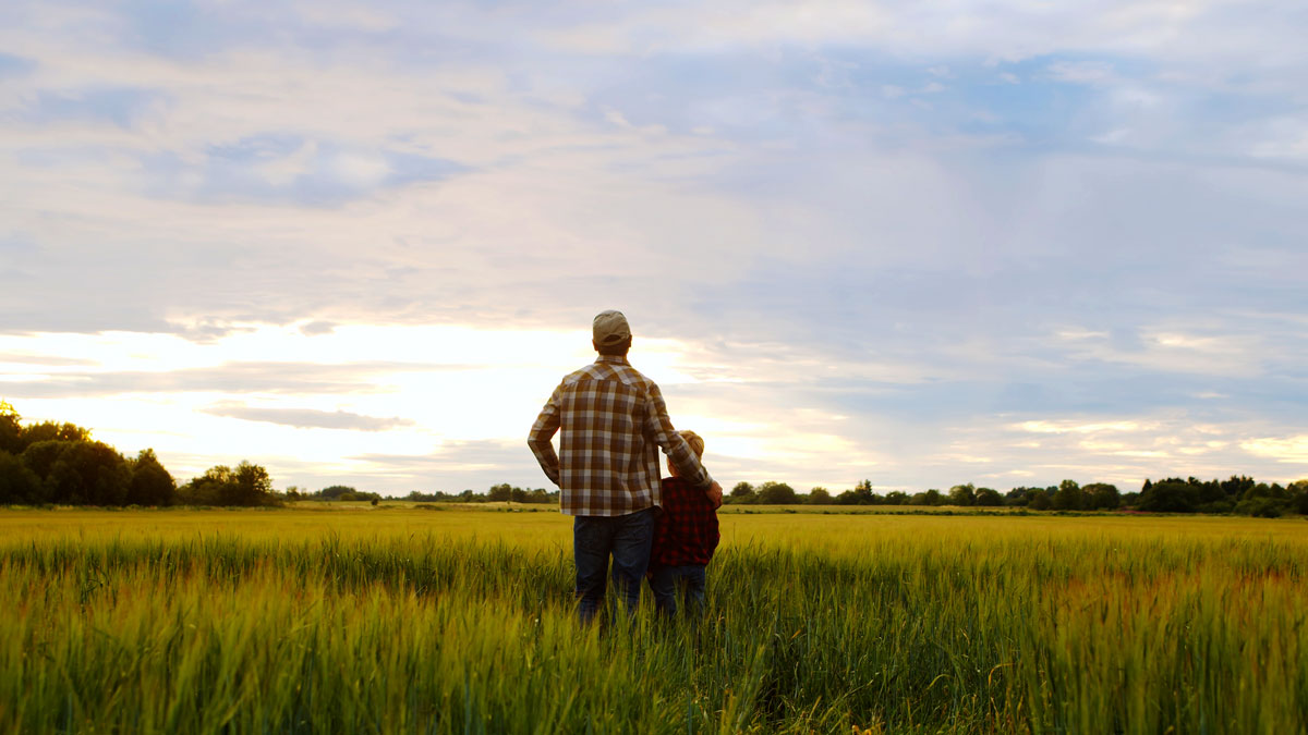 Farmer and his son in front of a farm landscape